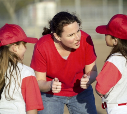 Woman coaching girl baseball players