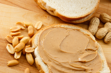 Peanut butter on a slice of bread with shelled and unshelled peanuts