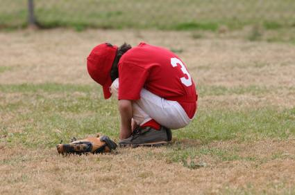 Youth baseball player crouching in sadness